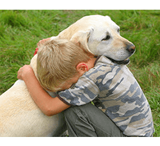 Young boy hugging his emotional support animal yellow labrador at park